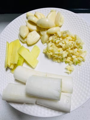 魚を焼いている間に、材料と付け合わせを準備します。
1. ニンニクはみじん切りにするか、そのままにしておきます。ショウガは薄切りにし、ネギは小口切りにします。パクチーと玉ねぎは洗って薄切りにします。

2. その他の付け合わせ（キャベツ、こんにゃく豆腐、豆腐シート、きのこなど）を洗って準備します。