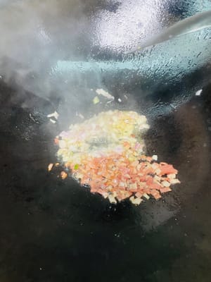 Aggiungere un altro cucchiaio d'olio, soffriggere la pancetta finché il grasso non si sarà sciolto, quindi aggiungere le cipolle tritate e soffriggere finché non saranno fragranti. Infine, aggiungere il kimchi e soffriggere a fuoco vivo per far sprigionare completamente il sapore aspro e piccante.