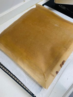 ケーキベースを冷まします。

焼き上がったら、ベーキングペーパーを網に敷きます。焼き上がったら網から取り出し、数回軽く叩いて余分な熱を逃がし、すぐに網にひっくり返します。天板を慎重に取り出します（熱いので注意してください）。次に、ベーキングペーパーをはがし、清潔なベーキングペーパーまたはベーキングマットをもう一枚重ねて覆います（水分の蒸発を防ぐためです。そうしないと、伸ばすときに割れてしまいます）。触っても熱くなくなるまで冷まします。冷めすぎないようにしてください。冷めすぎたケーキは脆くなり、伸ばすと割れてしまいます。

タオルのように簡単にケーキを巻けます！😀