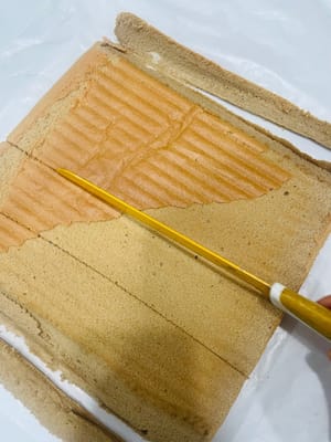 Dinginkan potongan kue, balikkan sisi depannya ke atas (untuk digulung nanti), lalu gunakan pisau untuk membuat beberapa potongan (tanpa memotong) agar mudah dibentuk saat digulung.
Permukaan kue saya jatuh, dan itu semua salah saya karena merobek kertas roti terlalu cepat dan kasar! Dan saat memanggang, saya melapisinya dengan kertas timah sebelum waktunya habis, yang juga memengaruhi kondisi permukaannya. Untungnya, kuenya digulung terbalik 😂