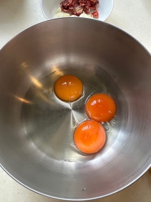 Comienza preparando la salsa para pasta. En un tazón grande, mezcla los huevos, la pimienta negra, el queso rallado y la mantequilla de pistacho hasta que estén bien integrados.