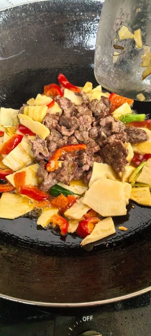 Das Rindfleisch dazugeben und kurz bei starker Hitze anbraten, dann mit gehackten Frühlingszwiebeln bestreuen.