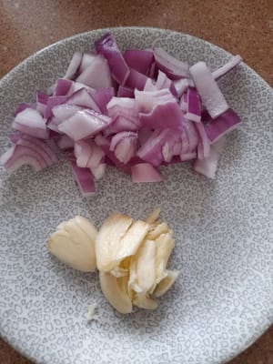 Zwiebel und Knoblauch waschen, zerdrücken und die Zwiebel würfeln.