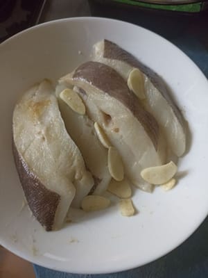 Den Heilbutt auf einen Teller legen und in Scheiben geschnittenen Knoblauch, 1/2 TL Pfefferpulver und 1/8 TL Salz hinzufügen.
