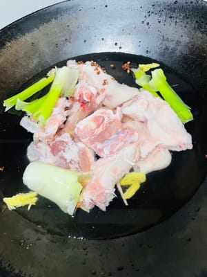 Blanchir les os d’agneau dans une casserole d’eau froide. Ajouter une grande quantité d’eau, 10 grains de poivre rouge, un demi-oignon vert (ou 2 oignons verts), 3 tranches de gingembre et 1 cuillère à soupe de sauce soja. Porter à ébullition à feu vif. Blanchir l’agneau 5 minutes. Retirer les os, rincer abondamment à l’eau tiède et égoutter.