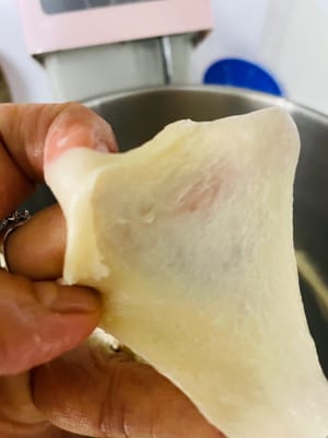 生地をスピード2で3分間こね、材料をなじませます。その後、スピード5～6でさらに6分間こね、生地が少しギザギザの膜状になるまでこねます（完璧を目指さないでください。これはまだ半完成の膜です）。バターと塩を加え、スピード2で3分間こねてバターを吸収させます。その後、スピード5～6でさらに8～10分間こね、「グローブフィルム」（破ったときに滑らかな縁を持つ薄く半透明の膜。柔らかいパンを作る秘訣です！）になるまでこねます。