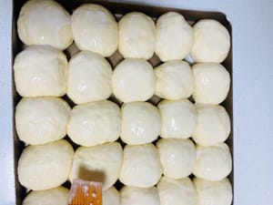 パンのデコレーション：ココナッツミルクで和える（オーブンも同時に予熱する）
発酵した生地を取り出し、ココナッツミルクを表面に均等に塗り広げ、余分なミルクはパンの縁にかけます。
白ゴマ（お好みで）とココナッツの細切りを散らせば、パンの完成です。
