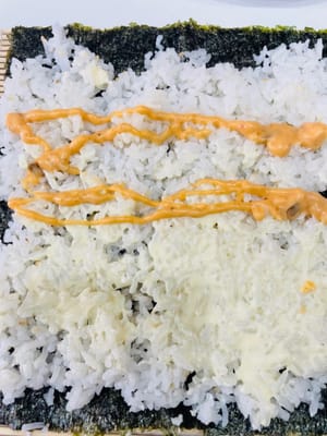 卷制寿司:
将卷帘平铺,紫菜光滑面朝下铺在卷帘上,均匀铺上拌好的米饭,用手轻压平整。挤上沙拉酱、千岛酱并抹匀,摆上蟹柳棒、蛋皮(或蛋丝)等食材。