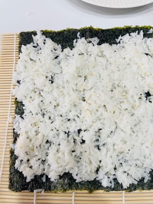 卷制寿司:
将卷帘平铺,紫菜光滑面朝下铺在卷帘上,均匀铺上拌好的米饭,用手轻压平整。挤上沙拉酱、千岛酱并抹匀,摆上蟹柳棒、蛋皮(或蛋丝)等食材。