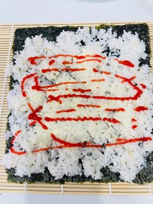 卷制寿司:
将卷帘平铺,紫菜光滑面朝下铺在卷帘上,均匀铺上拌好的米饭,用手轻压平整。挤上沙拉酱、千岛酱并抹匀,摆上蟹柳棒、蛋皮(或蛋丝)等食材。
