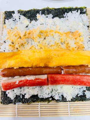 卷制寿司:
将卷帘平铺,紫菜光滑面朝下铺在卷帘上,均匀铺上拌好的米饭,用手轻压平整。挤上沙拉酱、千岛酱并抹匀,摆上蟹柳棒、蛋皮(或蛋丝)等食材。