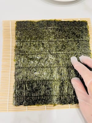 卷制寿司:
将卷帘平铺,紫菜光滑面朝下铺在卷帘上,均匀铺上拌好的米饭,用手轻压平整。挤上沙拉酱、千岛酱并抹匀,摆上蟹柳棒、蛋皮(或蛋丝)等食材。