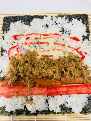 卷制寿司:
将卷帘平铺,紫菜光滑面朝下铺在卷帘上,均匀铺上拌好的米饭,用手轻压平整。挤上沙拉酱、千岛酱并抹匀,摆上蟹柳棒、蛋皮(或蛋丝)等食材。