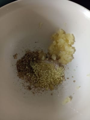 Hähnchenmarinade zubereiten: 2 fein gehackte Knoblauchzehen, 1/2 TL Salz, 1/2 TL Pfefferpulver, 1/2 TL Aroma, 1/2 TL Zucker, 1 TL Sesamöl
