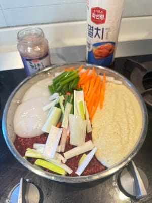 Dans un grand saladier, mélanger la poudre de piment rouge coréen, le mélange de riz gluant, le jus mixé, les poireaux, les carottes, le radis blanc et les fleurs de ciboulette.