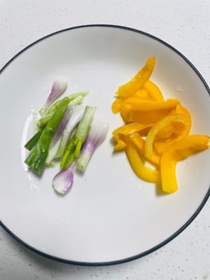 Tagliate i peperoni e i cipollotti a pezzetti e metteteli da parte. Inizialmente volevo usare dei peperoni rosso vivo per aggiungere colore al piatto e renderlo più accattivante, ma non riuscivo a trovarli in frigorifero, quindi ho dovuto usare dei peperoni gialli per