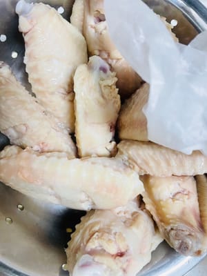 Secar las alitas de pollo: Toma papel de cocina y coloca las alitas una a una sobre él. Presiona y seca suavemente para secar la humedad superficial y evitar salpicaduras de aceite durante la fritura posterior.
