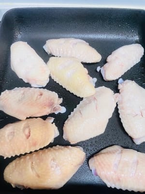 フライパンまたは中華鍋を弱火にかけ、少量の油をスプレーでひきます（刷毛で薄く塗るのも良いでしょう）。油が少し温まったら、鶏手羽先を入れ、弱火でじっくりと焼きます。時々ひっくり返し、両面が黄金色になり、香ばしくなるまで焼きます。