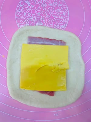 นำแป้งที่พักไว้แล้วมาคลึงให้เป็นรูปสี่เหลี่ยมจัตุรัสขนาดใหญ่กว่าชีสแผ่นเล็กน้อย

วางเบคอนหนึ่งชิ้นและชีสหนึ่งแผ่นลงบนแป้ง จากนั้นพับแป้งเฉียงๆ เหมือนห่อของชิ้นเล็กๆ ปิดปากแป้งให้แน่นเพื่อป้องกันไม่ให้ไส้ไหลออกมา