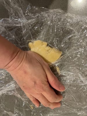 Coloque un trozo de film plástico en el fondo, ponga la bolita de mantequilla encima y cúbrala con otro trozo de film plástico. Aplana la masa de mantequilla con las manos.