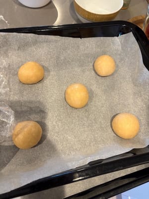 Coloque las bolas de masa pequeñas en una bandeja para hornear, dejando suficiente espacio en el medio de cada bola de masa, ya que las bolas de masa fermentarán y se expandirán nuevamente. Cubre también las bolas de masa con cáscara de piña.