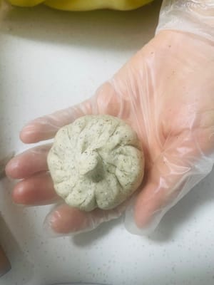 Preparazione dei Baozi:
1. Prendi una palla di impasto da 50 g, appiattiscila con il palmo della mano e arrotolala fino a formare una sfoglia rotonda con un centro spesso e bordi sottili.
2. Disponi una porzione di ripieno al sesamo nero al centro della sfoglia. Richiudi i bordi e stringili bene per evitare che si crepino durante la cottura a vapore.
3. Metti l'impasto avvolto nel cestello per la cottura a vapore e lascialo lievitare finché non raddoppia di volume.