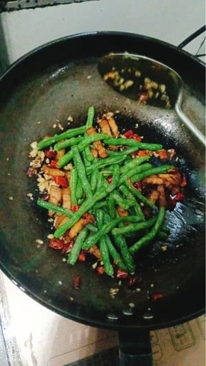 Pfanne erhitzen und Öl hinzufügen. Pfefferkörner, gehackten Knoblauch und getrocknete Chilischoten hinzufügen und anbraten, bis alles duftet. Schweinebauch hinzufügen und zweimal anbraten. Grüne Bohnen hinzufügen und gleichmäßig anbraten. Gewürze wie Sojasauce, Salz und Zucker hinzufügen, zweimal anbraten und vom Herd nehmen.