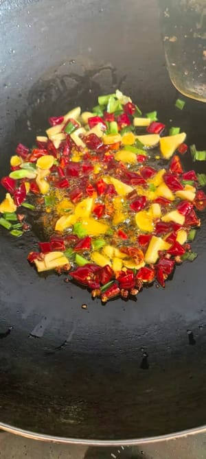 Frühlingszwiebeln, Ingwer, Knoblauch und getrocknete Chilischoten hinzufügen, unter Rühren anbraten, bis es duftet, dann Gurke und gewürfelte Karotten dazugeben.