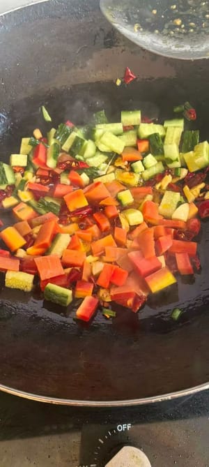 Frühlingszwiebeln, Ingwer, Knoblauch und getrocknete Chilischoten hinzufügen, unter Rühren anbraten, bis es duftet, dann Gurke und gewürfelte Karotten dazugeben.