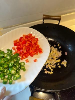 Anschließend rote und grüne Chilischoten hinzufügen und weiter rühren, bis sie weich sind.