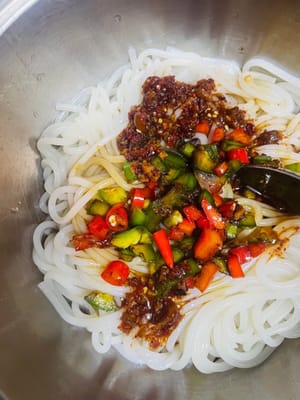 Mettete i noodles di riso in un contenitore capiente. Aggiungete prima 1 cucchiaio di olio al peperoncino e 2 cucchiai di salsa di soia. Quindi, prelevate un cucchiaio di olio piccante ottenuto versando a filo olio di sesamo caldo e peperoncini verdi e rossi tritati. Mescolate bene. Ogni noodles di riso è ricoperto dalla salsa oleosa, l'aroma è così invitante che farà bussare alla porta i vicini! Aggiungete il ravanello essiccato saltato in padella e le arachidi fritte, e infine cospargete con coriandolo e cipollotti tritati. Mescolate bene ed è pronto da mangiare! L'aroma è così forte che vi lascerà a bocca aperta; ogni boccone è autentico sapore di Nanchang!