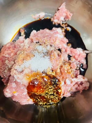 Préparez la farce de base à base de viande : ajoutez le sel, le bouillon de poulet, le sucre, la sauce soja, la sauce aux huîtres et le poivre au porc haché et mélangez bien.