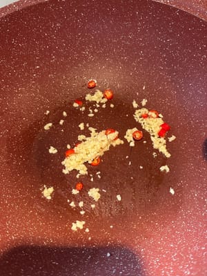 Dans une poêle chauffée avec de l'huile, commencez par faire revenir l'ail haché et les petits piments rouges