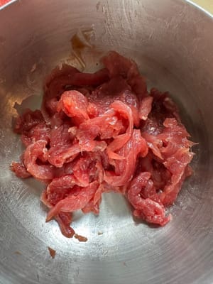 Pendant ce temps, coupez le bœuf en fines tranches et faites-le mariner avec du sucre, du poivre blanc, 1 cuillère à soupe de sauce soja, 1/2 cuillère à soupe de sauce aux huîtres et de la fécule de maïs